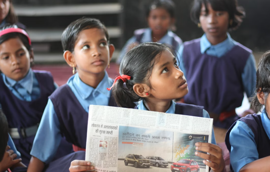 This image shows a child holding a newspaper in a classroom.