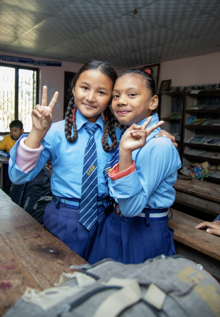 This photo shows two school girls in uniform showing a peace sign.